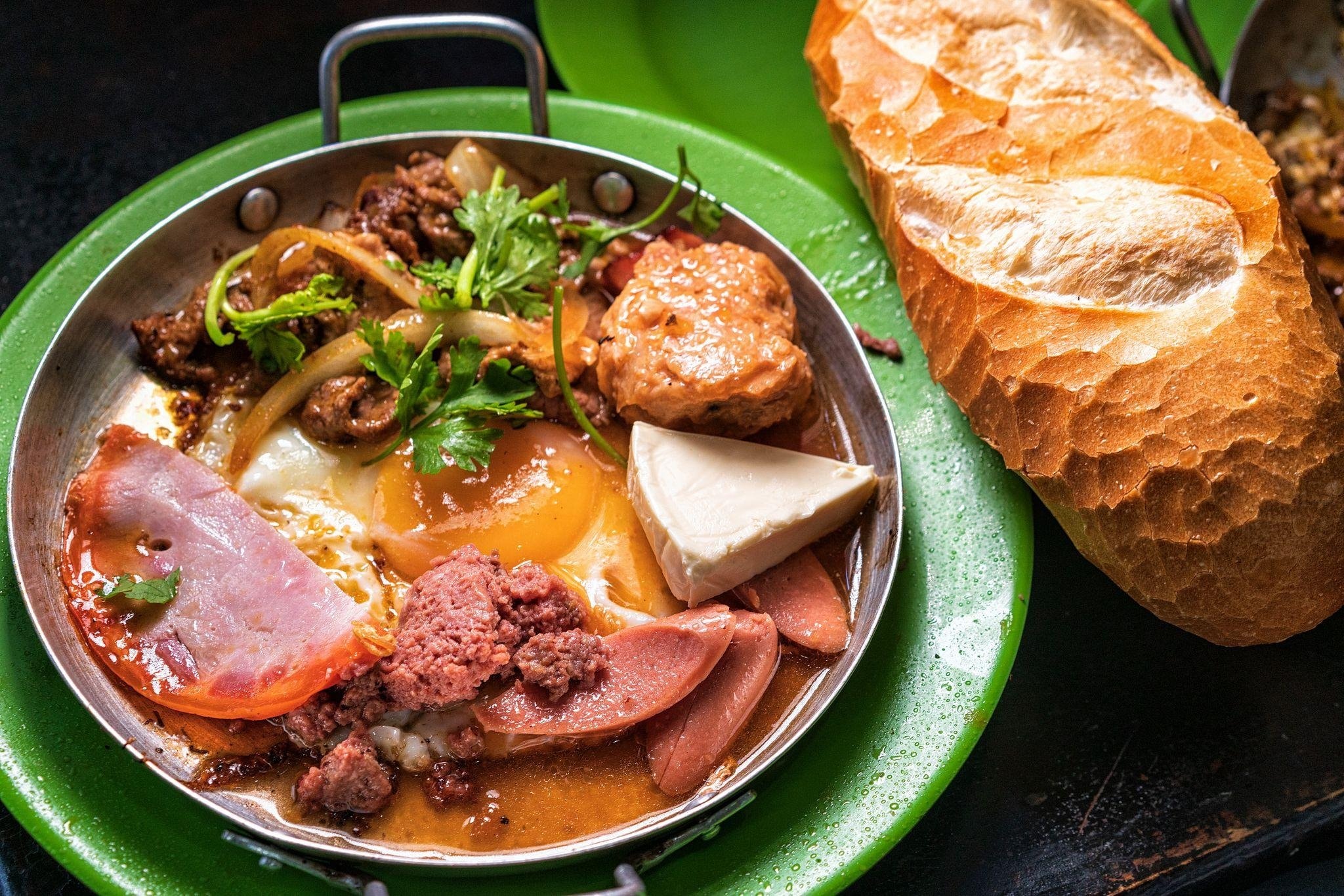 In a sizzling pan, ingredients like eggs, sausage, pâté, ham, or beef are cooked with butter and topped with a flavorful sauce
